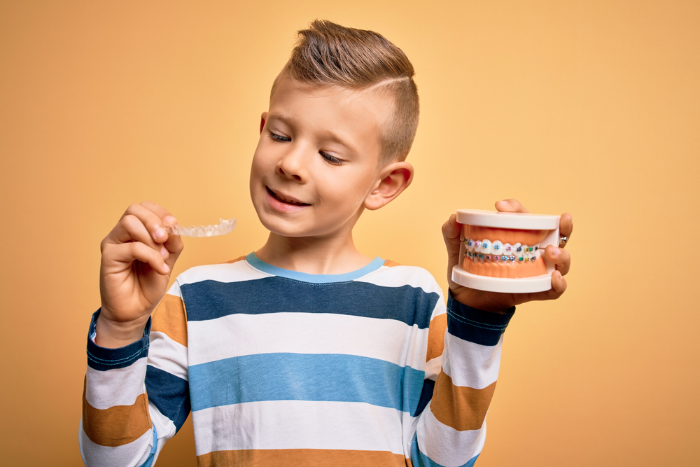 Child holding up braces and Invisalign